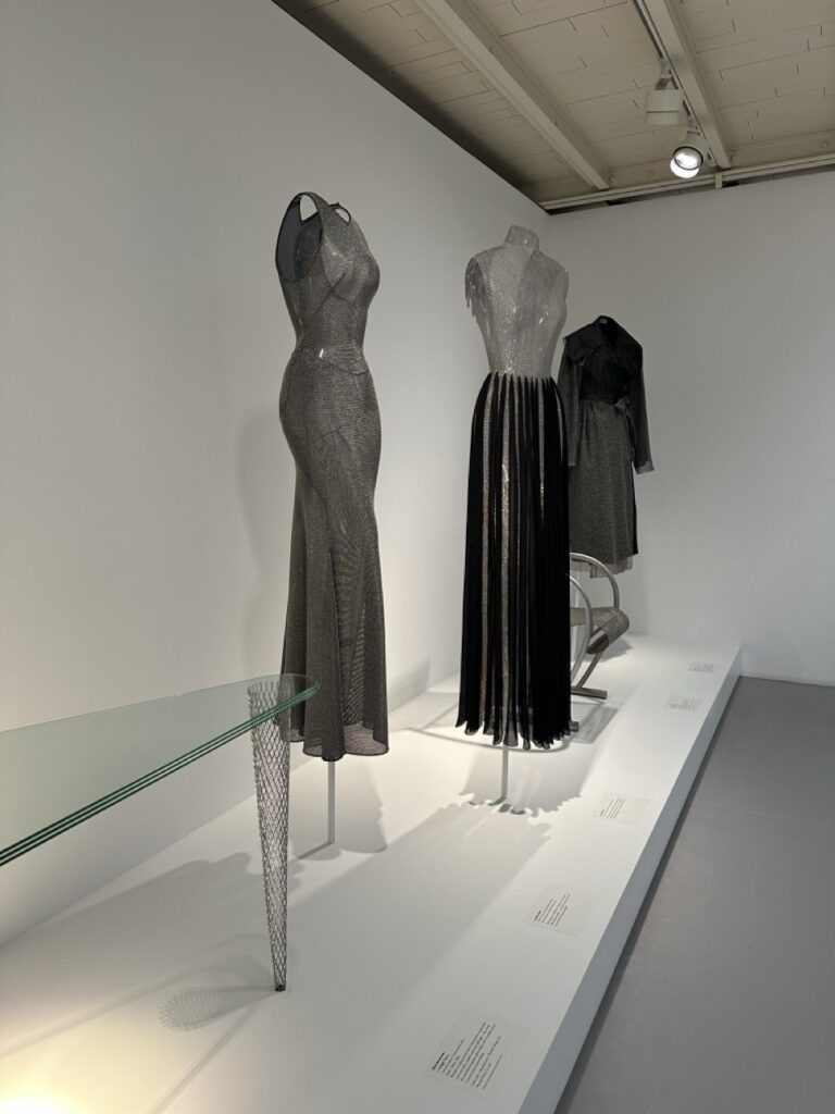 Glass table by Shiro Kuramata next to metallic gowns by Alaïa.