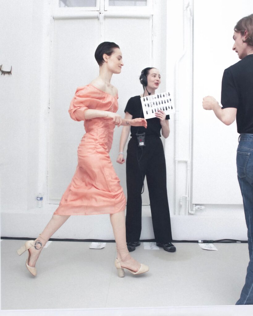 Backstage moment featuring a coral ruched dress and nude block heels from Lemaire Spring-Summer 2025 collection.
