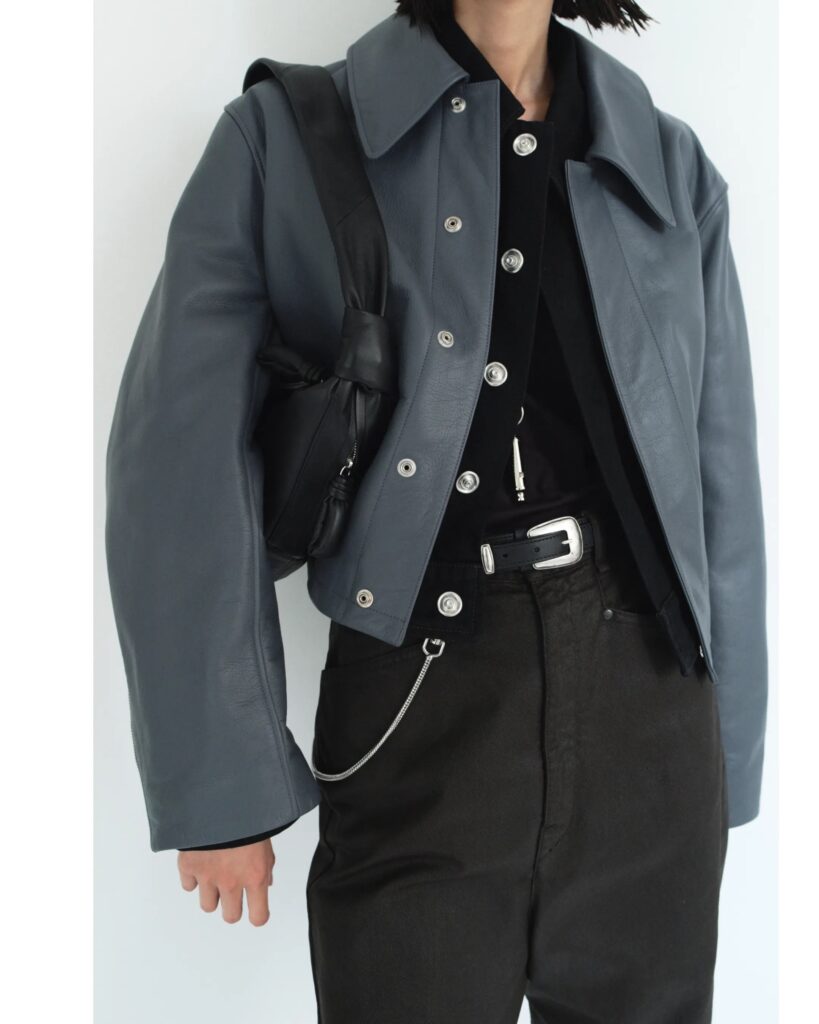 Model in slate gray leather jacket with black pants and minimalist accessories from Lemaire Spring-Summer 2025 collection.