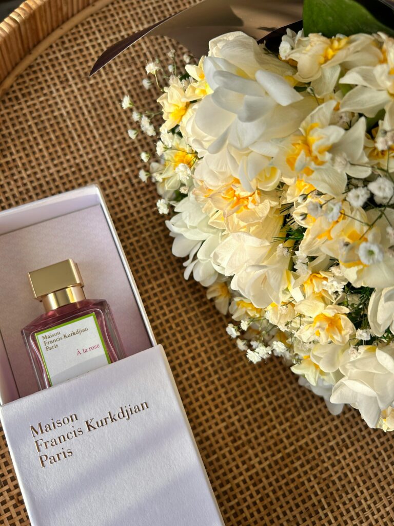 Maison Francis Kurkdjian À la Rose perfume bottle placed next to a floral arrangement.