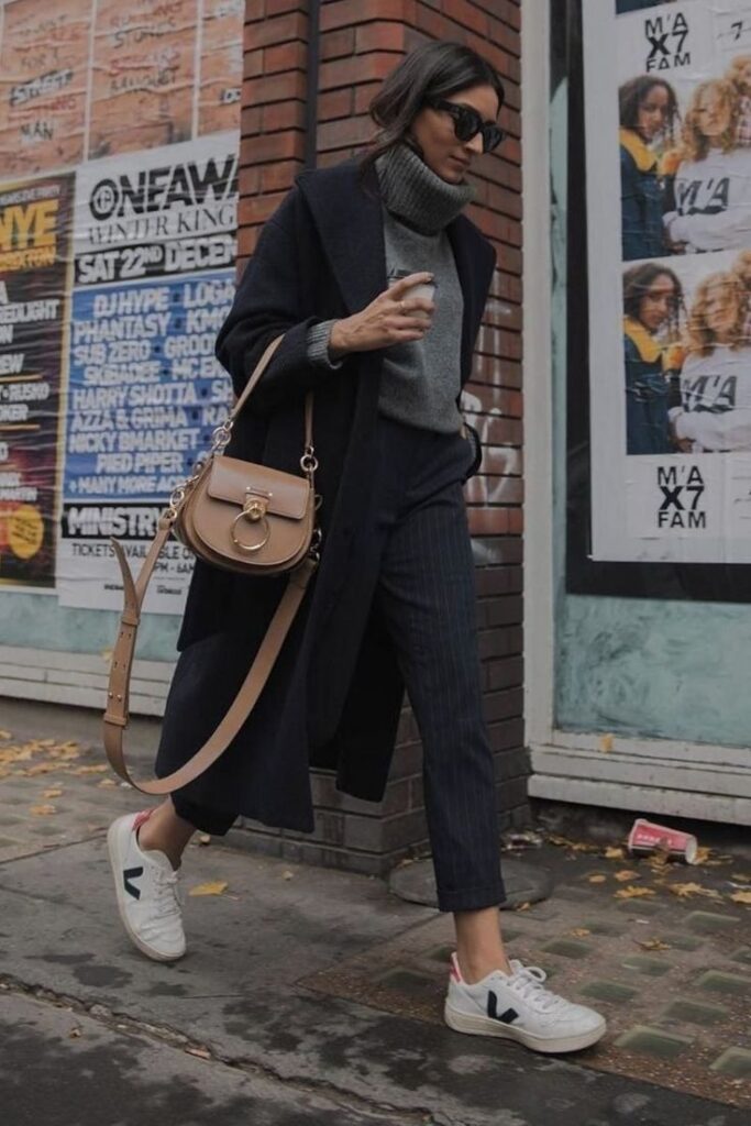 A woman styling white Veja sneakers, a must-have French sneaker brand, with a dark coat and tailored pants.
