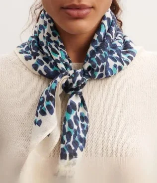 A close-up of a silk scarf with a blue and white leopard print from Eric Bompard, draped elegantly around the neck.