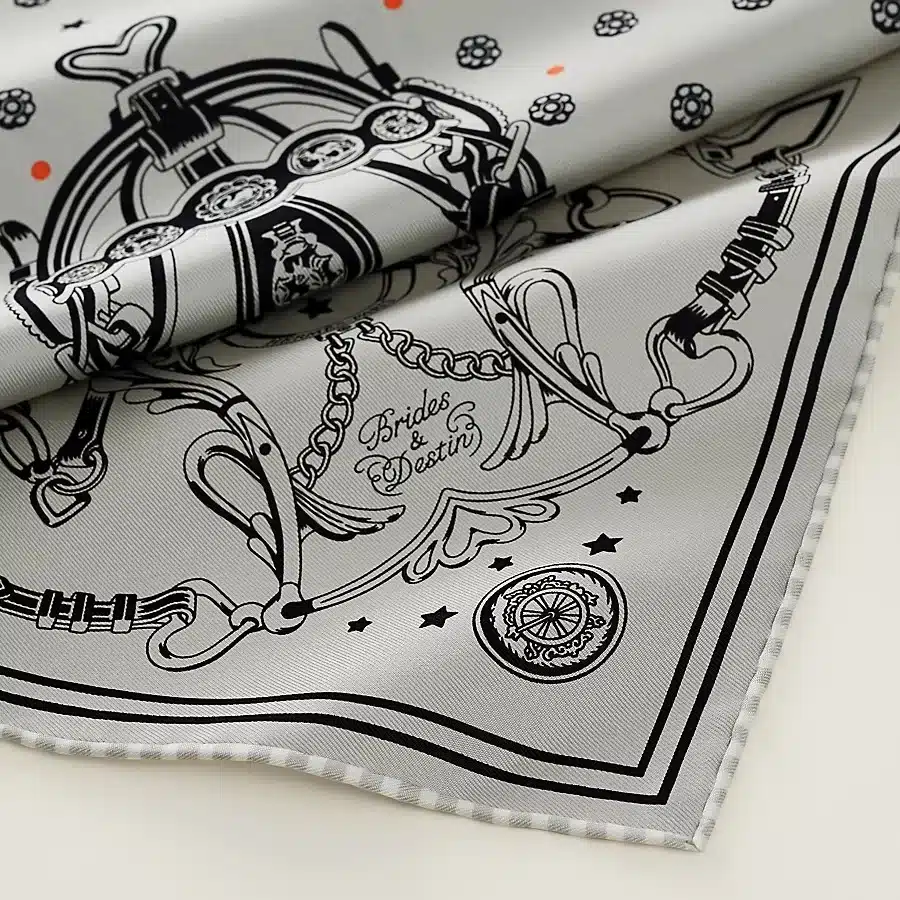 A detailed close-up of the Hermès Brides et Destin silk scarf featuring intricate equestrian-inspired motifs in black and white.
