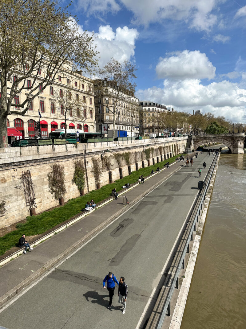 People walking and lounging on the pedestrianized banks of the Seine on a sunny April day in Paris