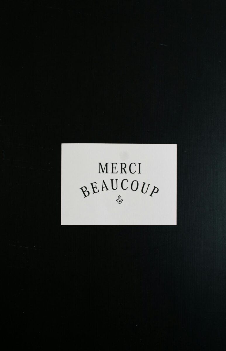 White card with the words “Merci Beaucoup” placed on a black background, symbolizing French politeness and etiquette