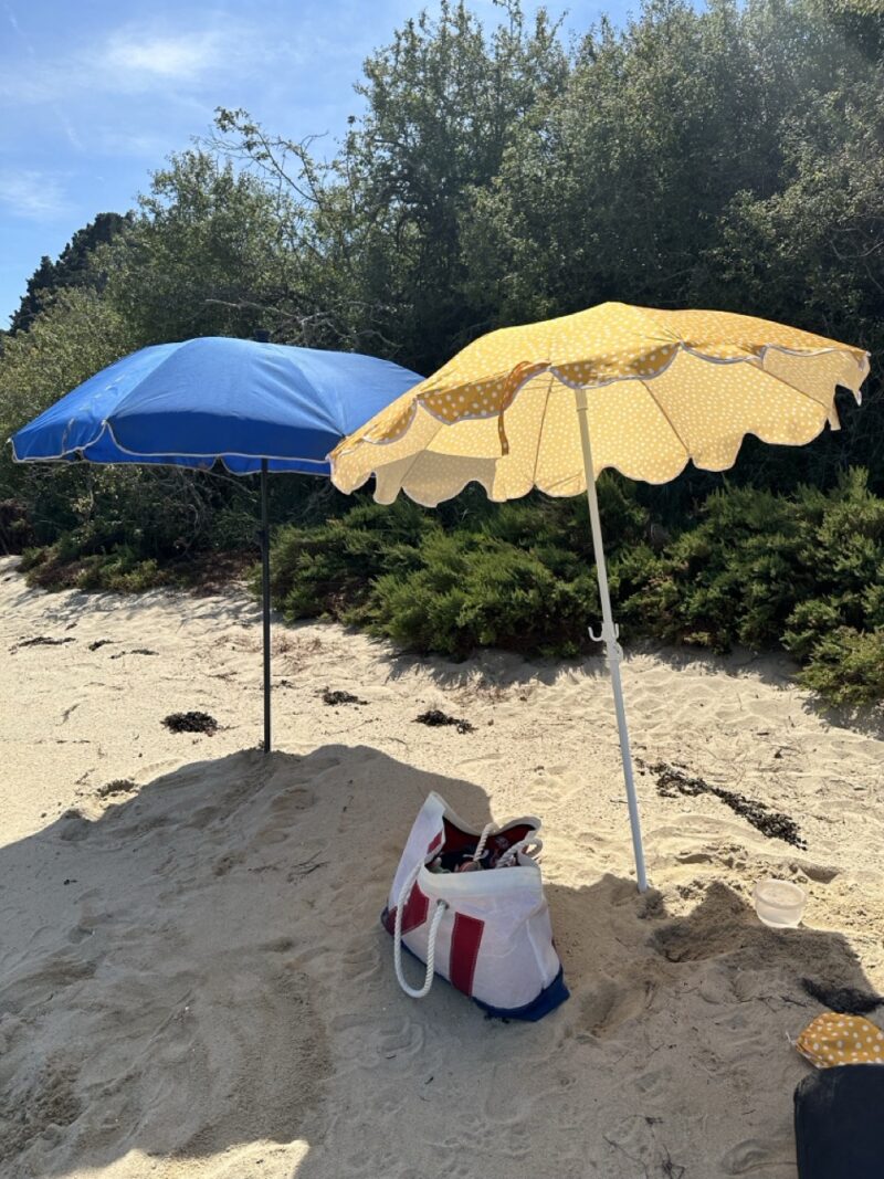 A sandy beach with yellow and blue parasols, a straw tote, and children's beach toys—classic French summer vacation