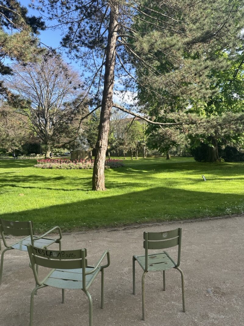 Empty green café chairs in a peaceful, sun-dappled Paris park in summertime