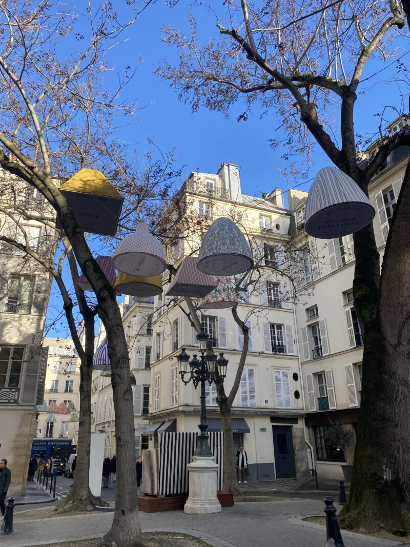 Art installation with lampshades hanging from trees in Place de Furstenberg