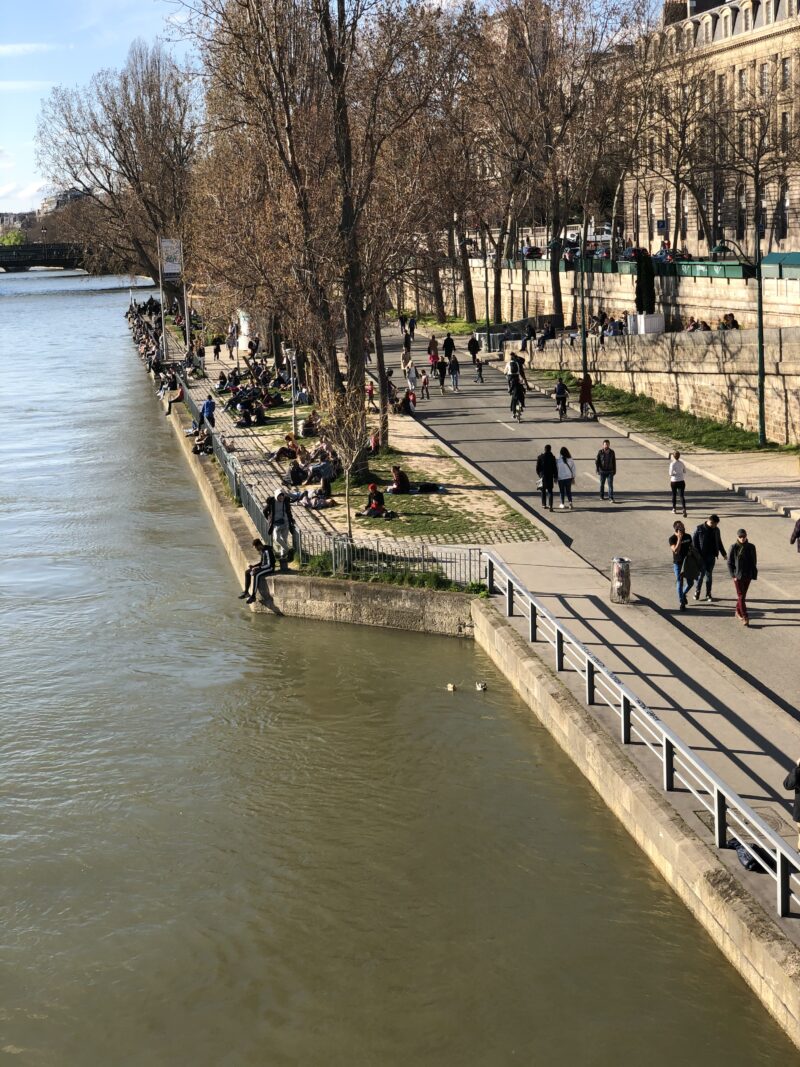 People walking along the Seine river in Paris on a bright March day