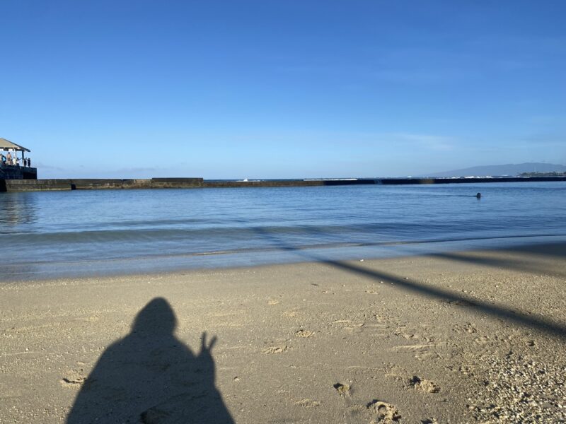 A shadow of a woman holding a peace sign on an empty beach during vacation