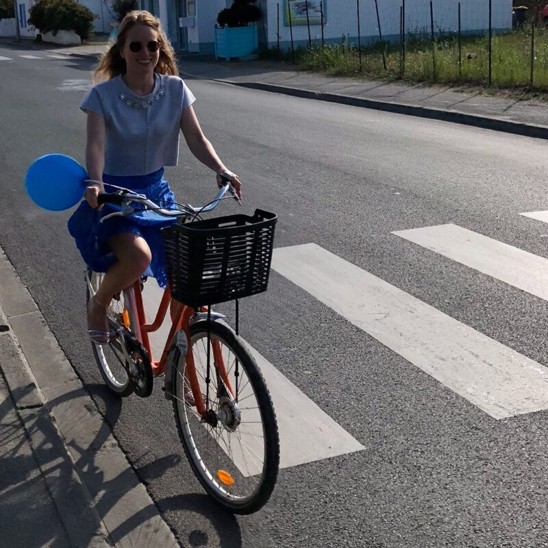 Pamela riding a bicycle in a blue skirt on Île d’Yeu on her way to a French wedding cocktail