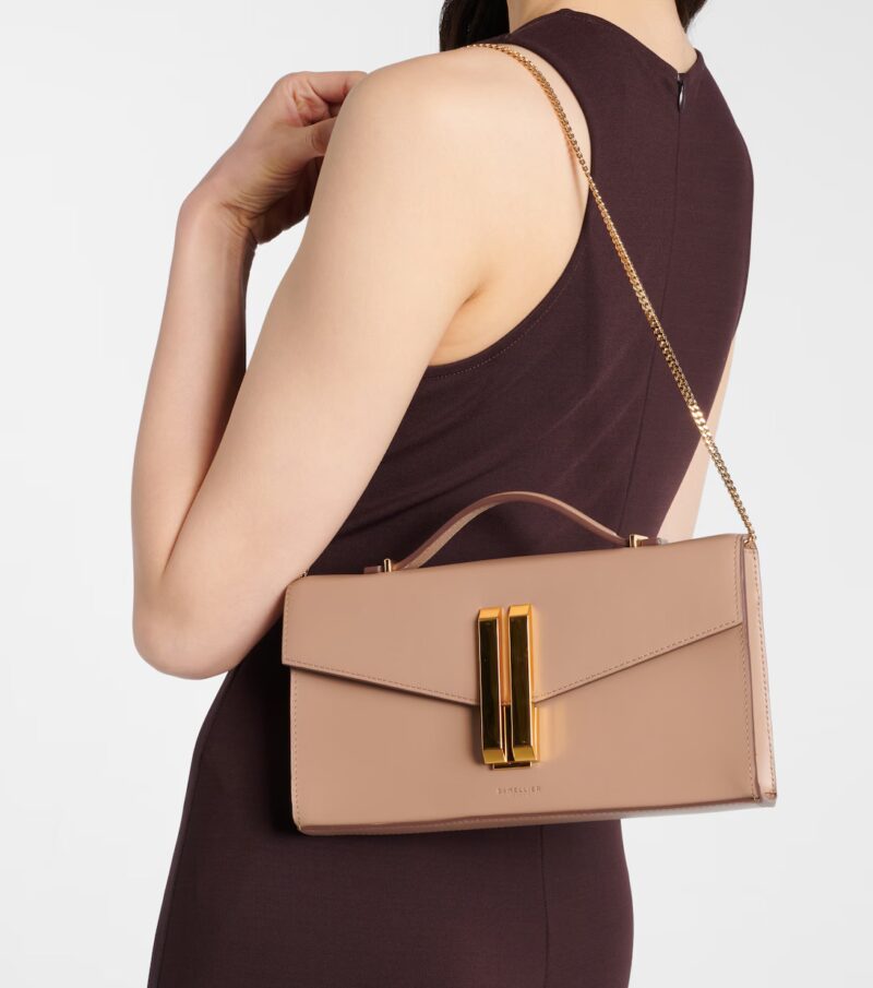 Woman wearing a burgundy dress and carrying a taupe DeMellier Vancouver clutch with gold clasp