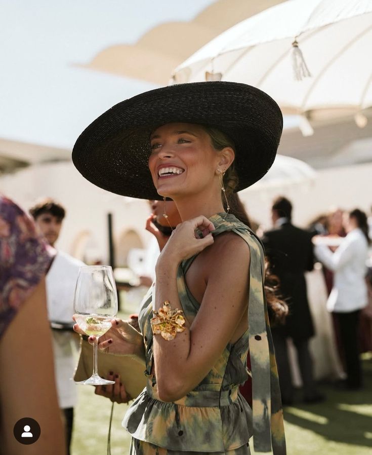 Woman in a printed dress and oversized black hat at an outdoor wedding