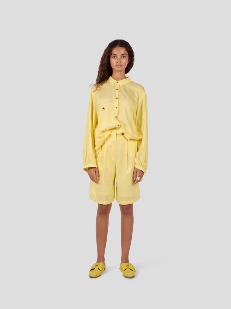 Model wearing yellow striped bermuda shorts and shirt set by Heimstone, a Parisian brand like Sézane