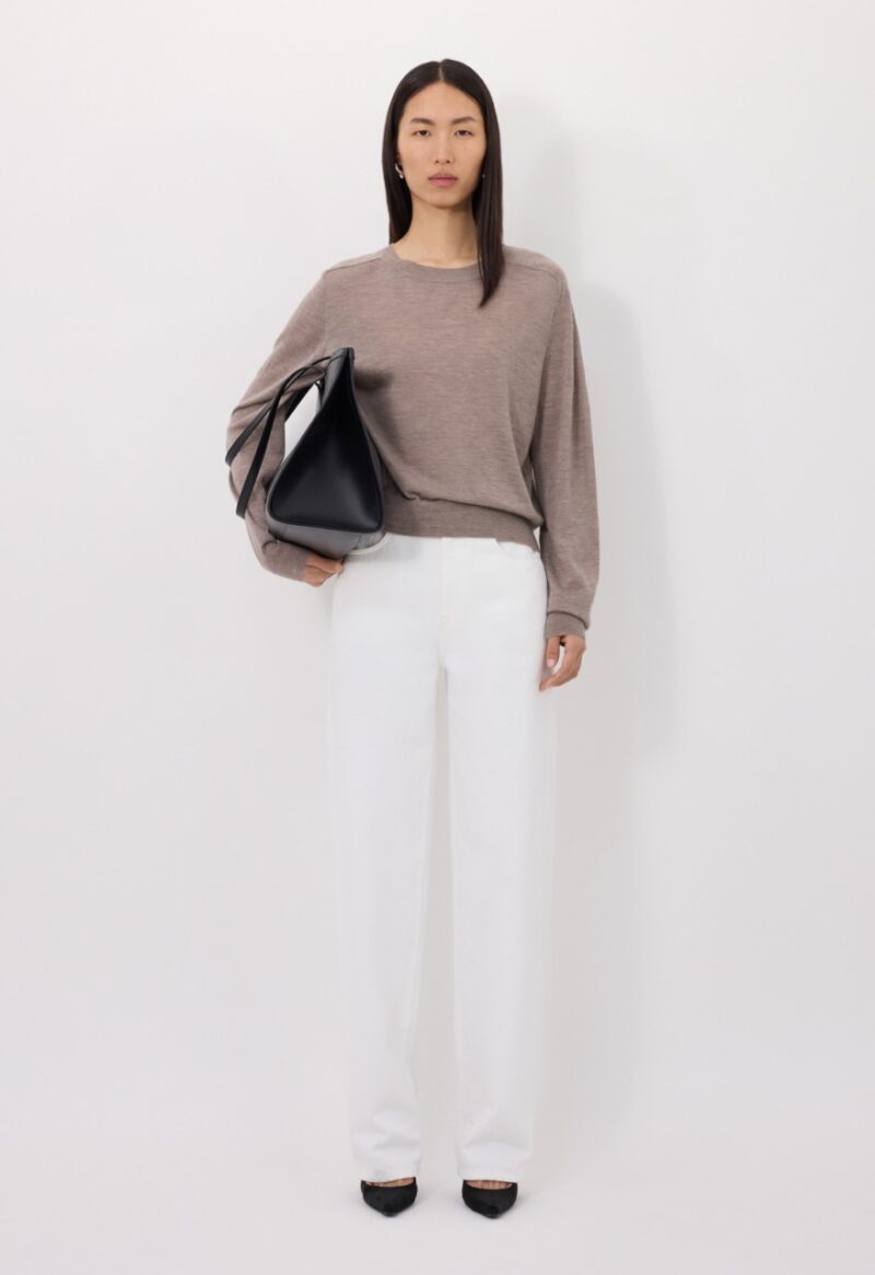 Model wearing neutral sweater and white trousers by Loulou Studio, one of the brands like Sézane