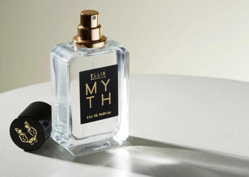 Ellis Brooklyn Myth perfume bottle with gold accents and black label, photographed on a neutral surface with its cap beside it