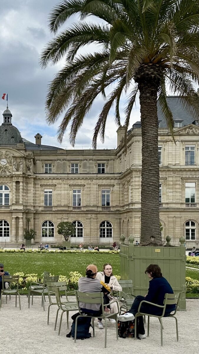 A group of people talking under a palm tree at Jardin du Luxembourg in Paris, illustrating quiet conversation and relaxed French etiquette