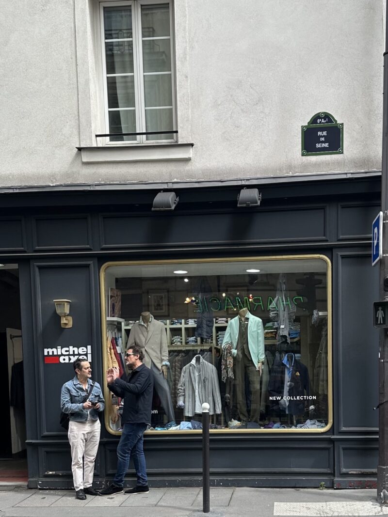 Two men talking in front of a boutique on Rue de Seine in Paris — a casual moment that hints at unspoken French social rules