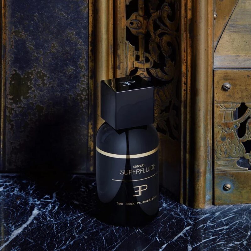 Black bottle of Les Eaux Primordiales Santal Superfluide placed on a marble and brass background