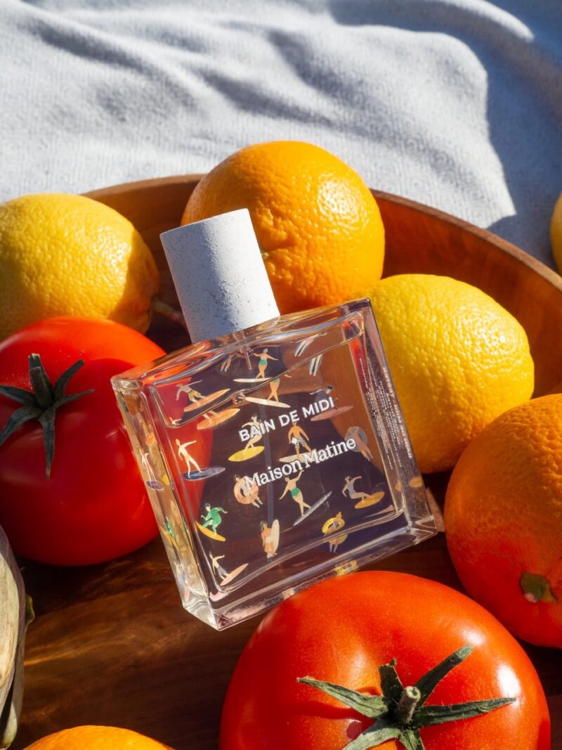 Maison Matine's Bain de Midi perfume bottle surrounded by fresh oranges and tomatoes, symbolizing a clean French non-toxic fragrance
