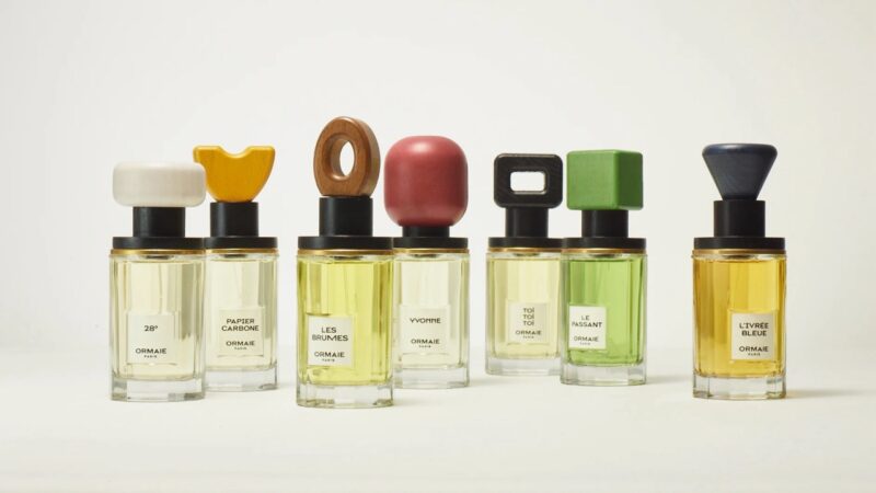 Ormaie perfume bottles in a row with colorful sculptural caps on a light background