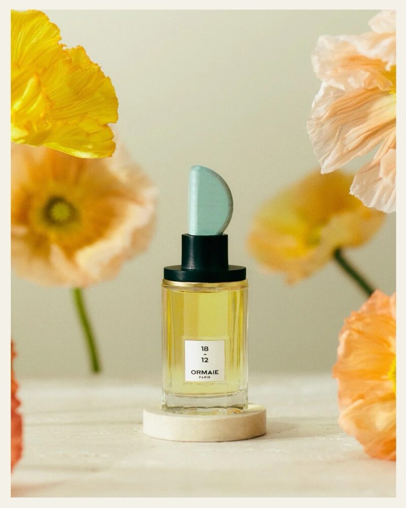 Perfume bottle illuminated by soft light with orange flowers, representing the warm, spicy, and gourmand layers of fragrance by notes