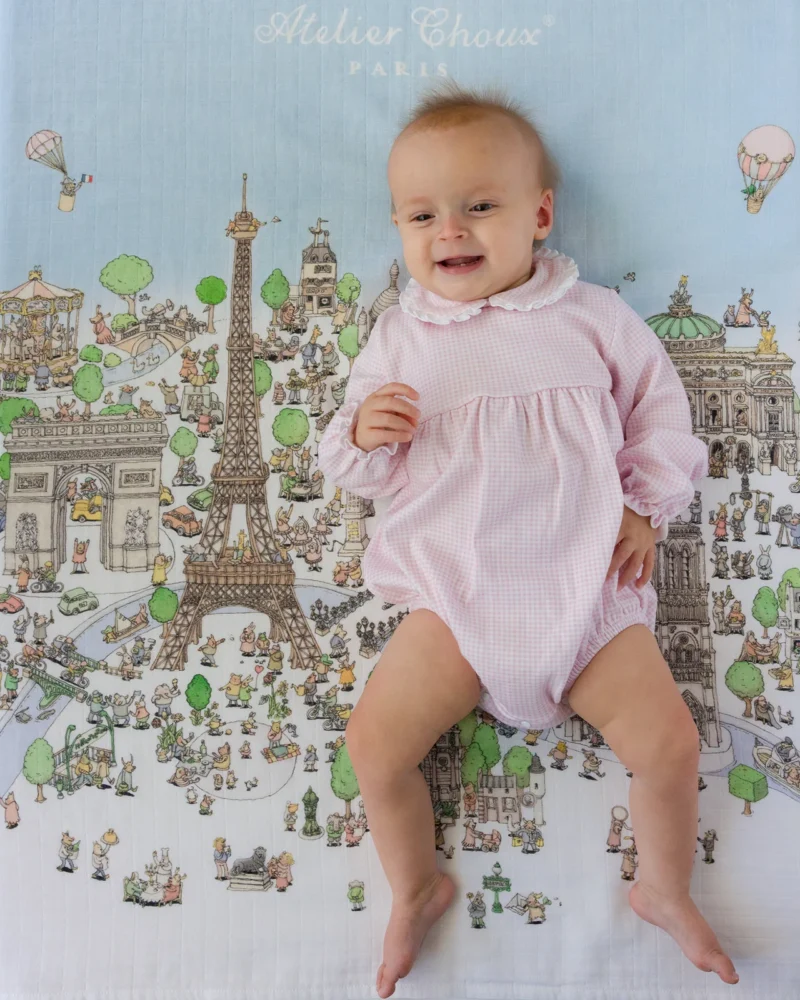 Baby wearing a pink romper by Atelier Choux, a whimsical French baby clothing brand.