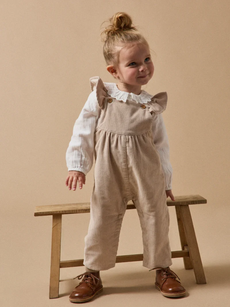 Baby girl in light-colored overalls by Cyrillus, part of French baby clothing brands.