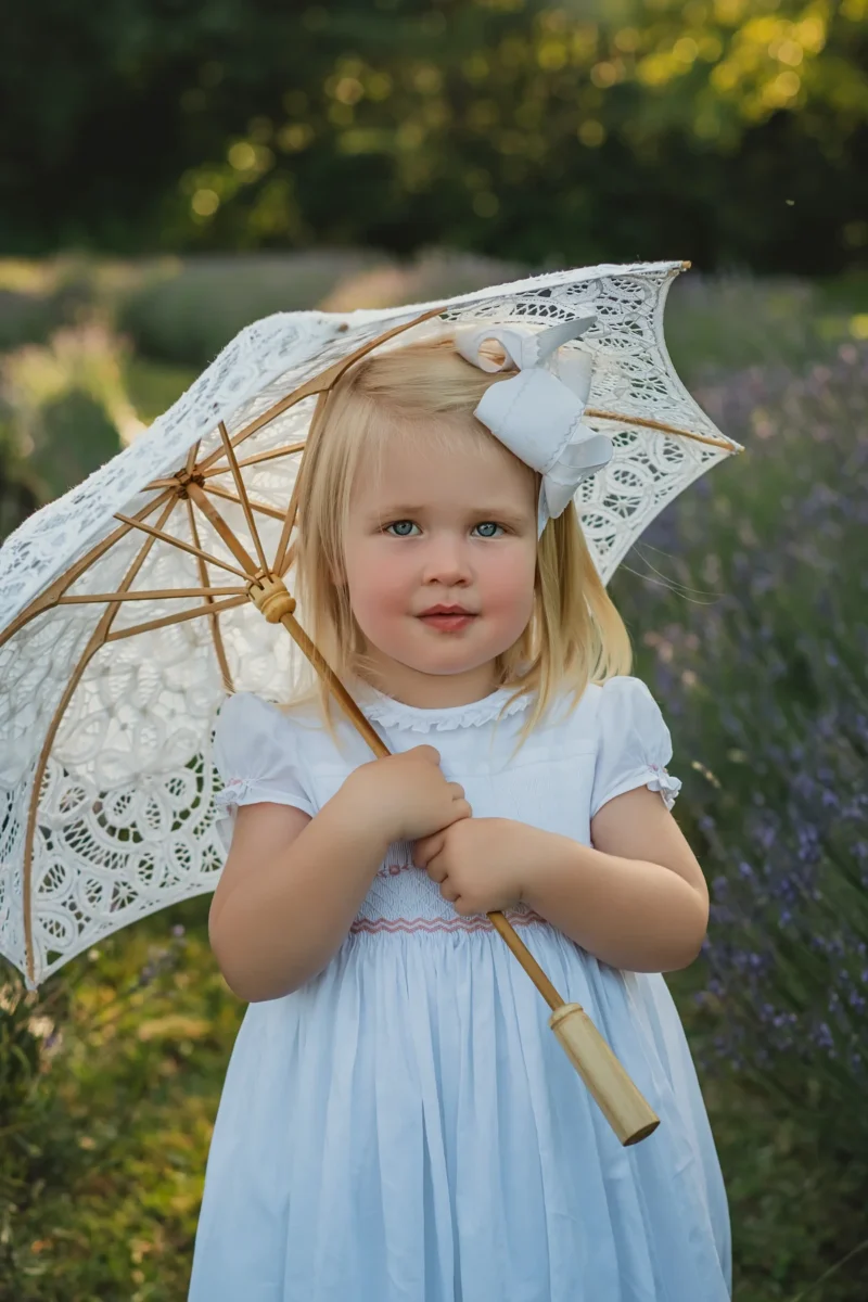 Baby girl in a lavender smocked dress by L’Île aux Fées, a French baby clothing brand.