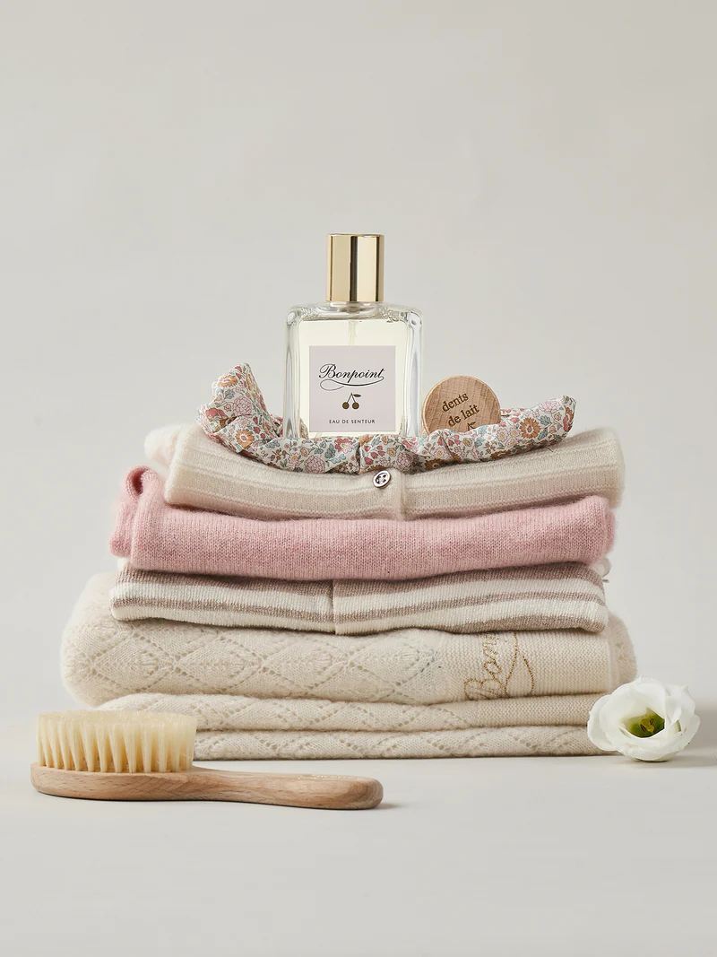 Stack of Bonpoint baby knitwear with eau de senteur and brush