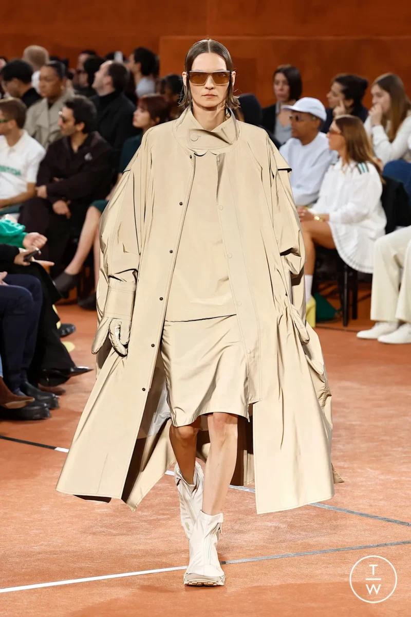 Cape-style coat from Lacoste runway, practical layering for rain outfits in Paris.
