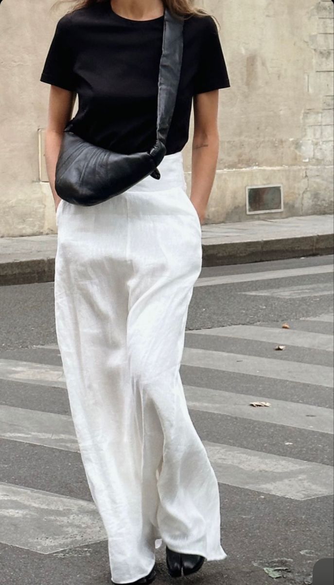 Woman in black t-shirt and white trousers wearing a small crossbody Parisian handbag.