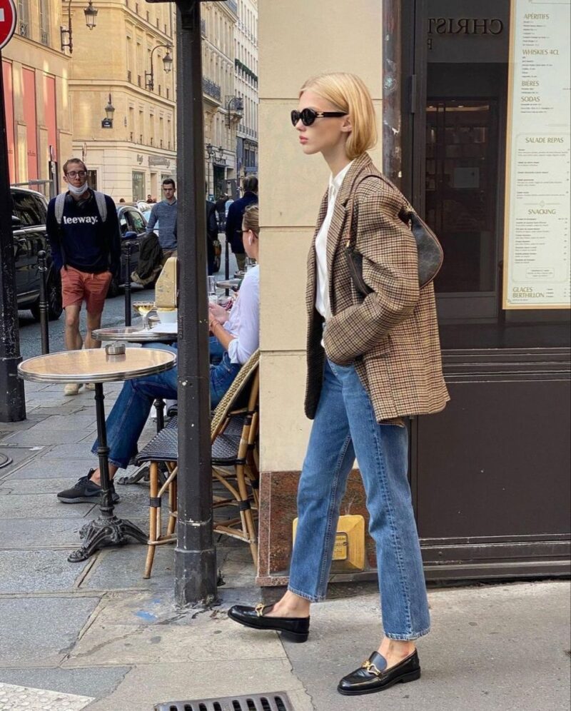 Parisian woman in blazer and jeans carrying a structured shoulder handbag.