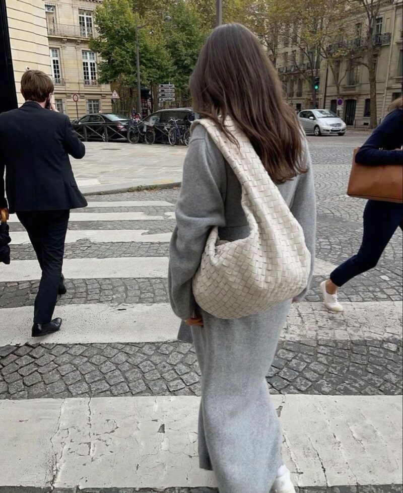 Woman in Paris wearing oversized blazer and sunglasses with a Parisian handbag, captured in a chic street style look.