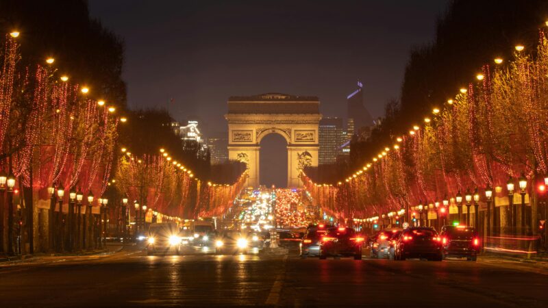 Arc de Triomphe at night with red Christmas lights along the Champs-Élysées in Paris.