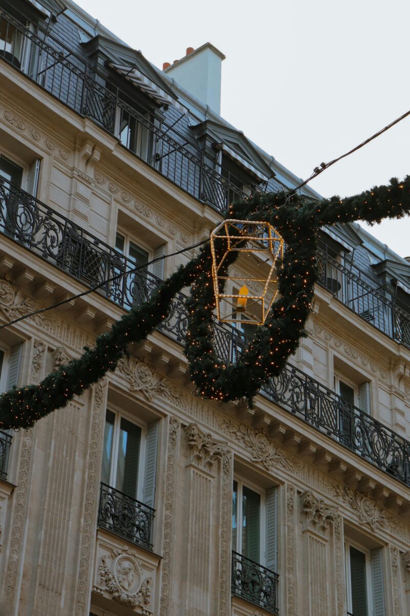 Haussmann building in Paris decorated with evergreen garlands and lights during the holiday season.