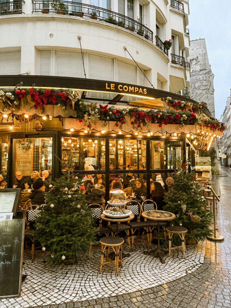 Café Le Compas in Montorgueil, Paris, decorated with garlands, red berries, and Christmas trees during the holidays.