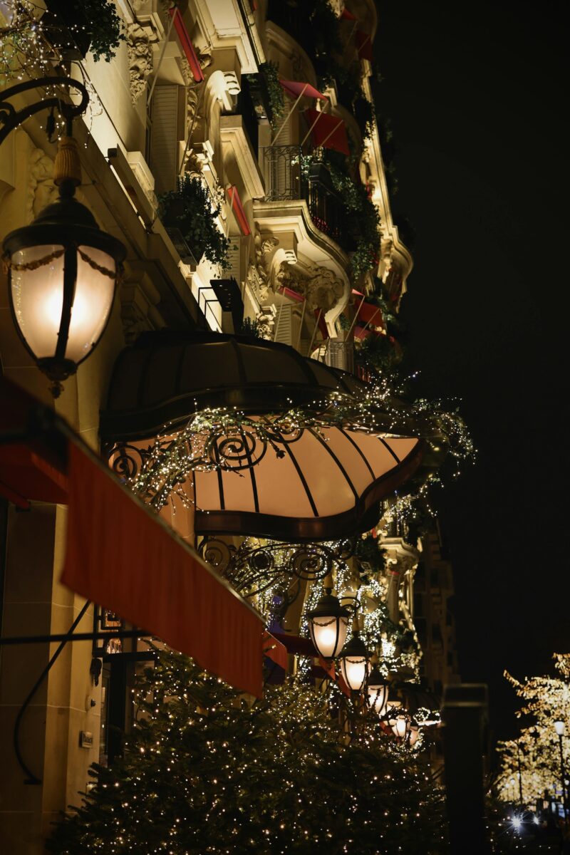 The facade of Le Plaza Athénée hotel on Avenue Montaigne, Paris, illuminated with Christmas trees and sparkling lights at night.