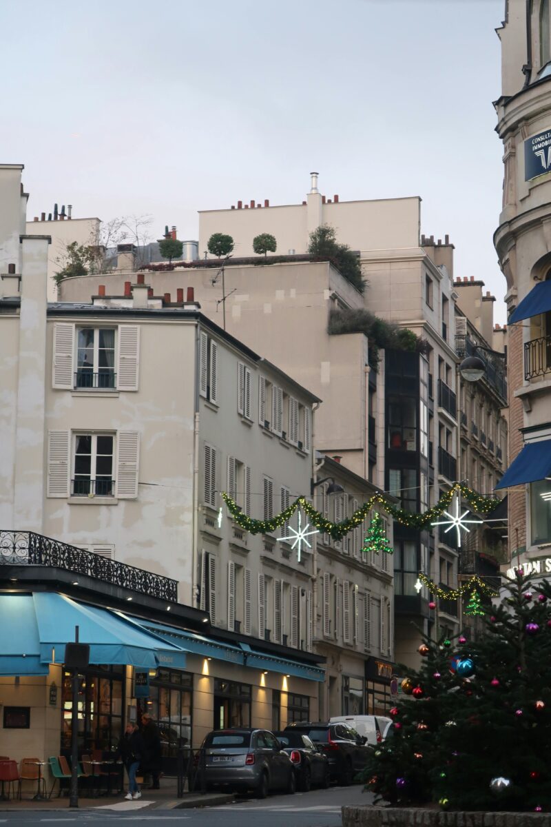 Christmas lights and garlands above a Parisian street with festive decorations and a Christmas tree.