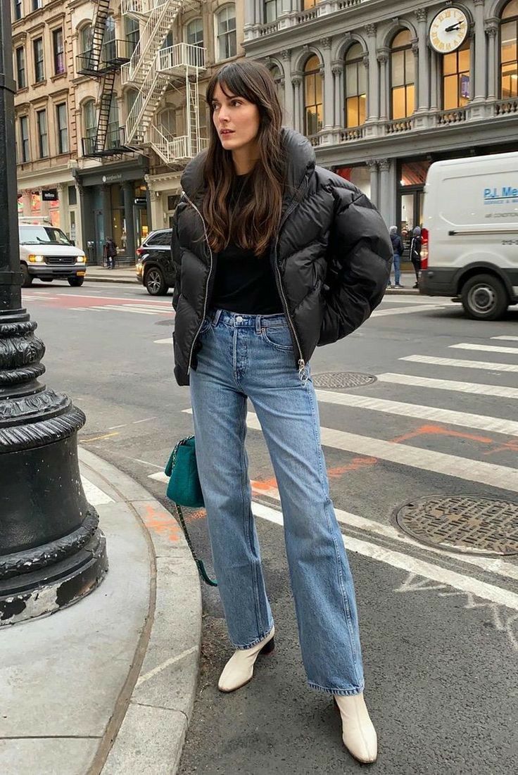 Woman wearing a black puffer jacket, straight-leg jeans, and white ankle boots — modern Paris winter outfit.