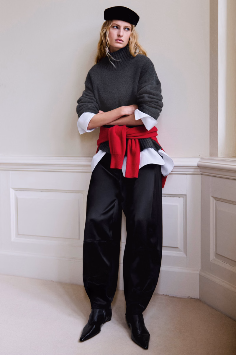 Model in a COS charcoal cashmere turtleneck sweater with a red sweater tied at the waist and black satin trousers